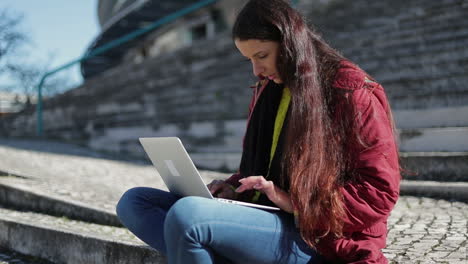 Focused-mature-woman-with-long-dark-hair-using-laptop-outdoor